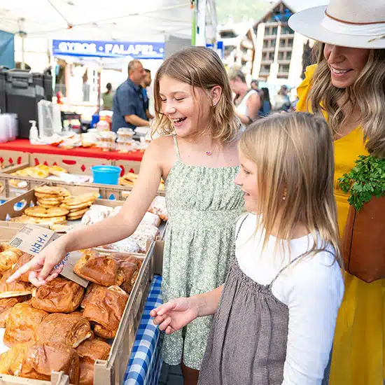 Two young girls and a woman admiring pastries at the Vail Farmers' Market & Art Show