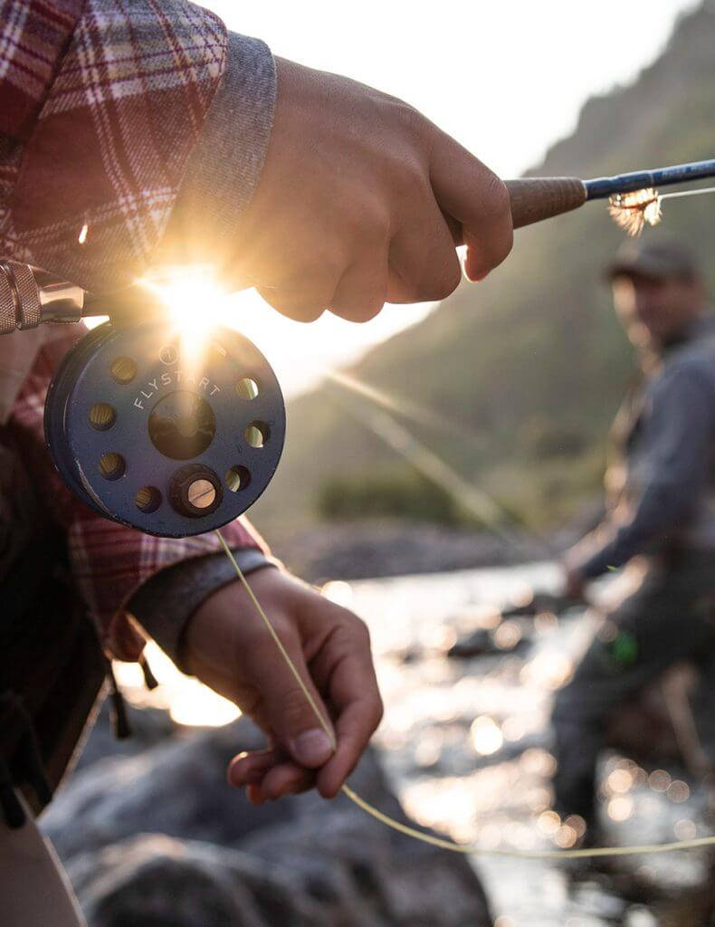 A man is holding a fly rod while fishing in a river in Vail.