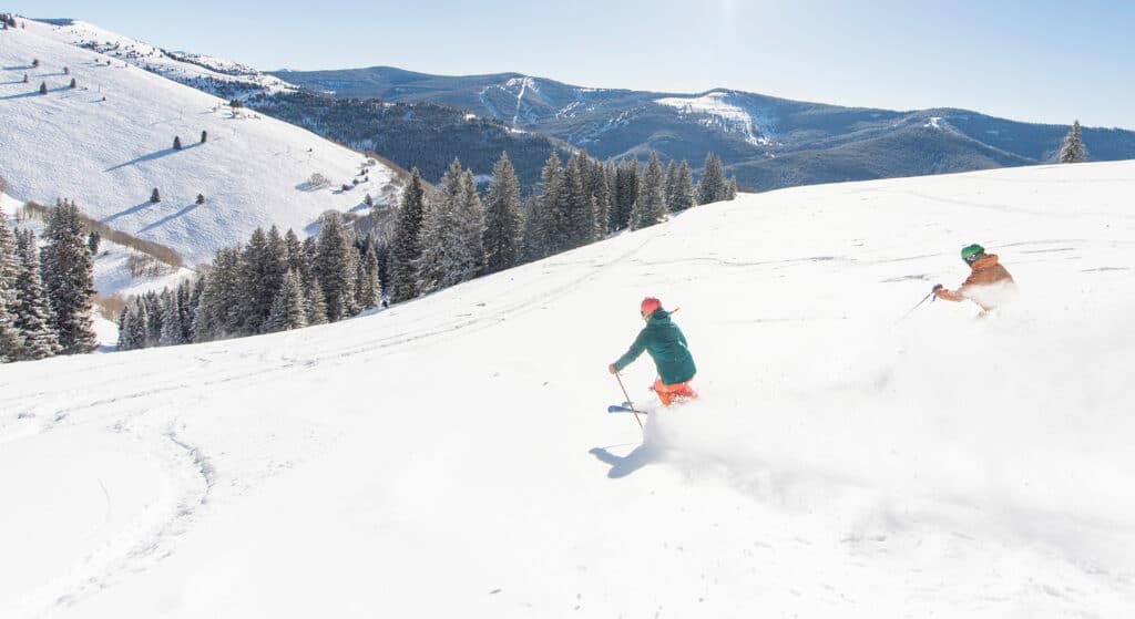 Two people skiing down a snowy slope in Vail.