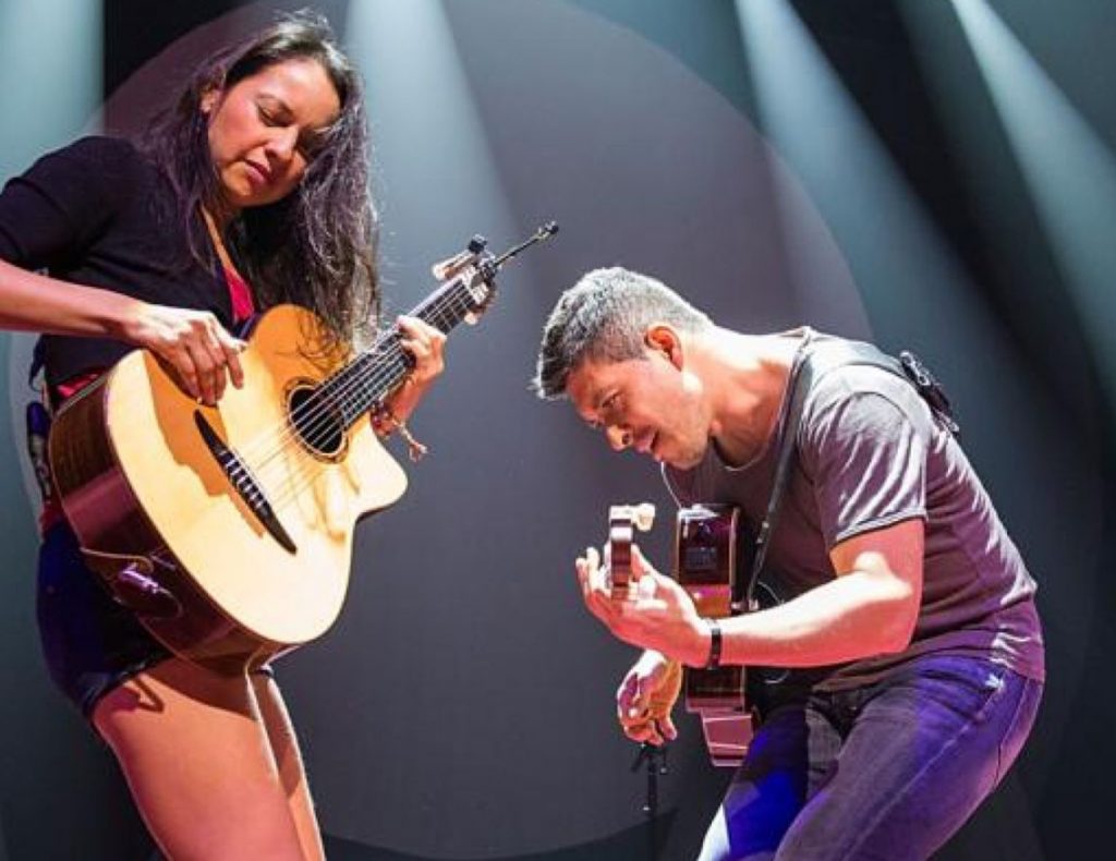 A man and a woman playing guitar on stage.
