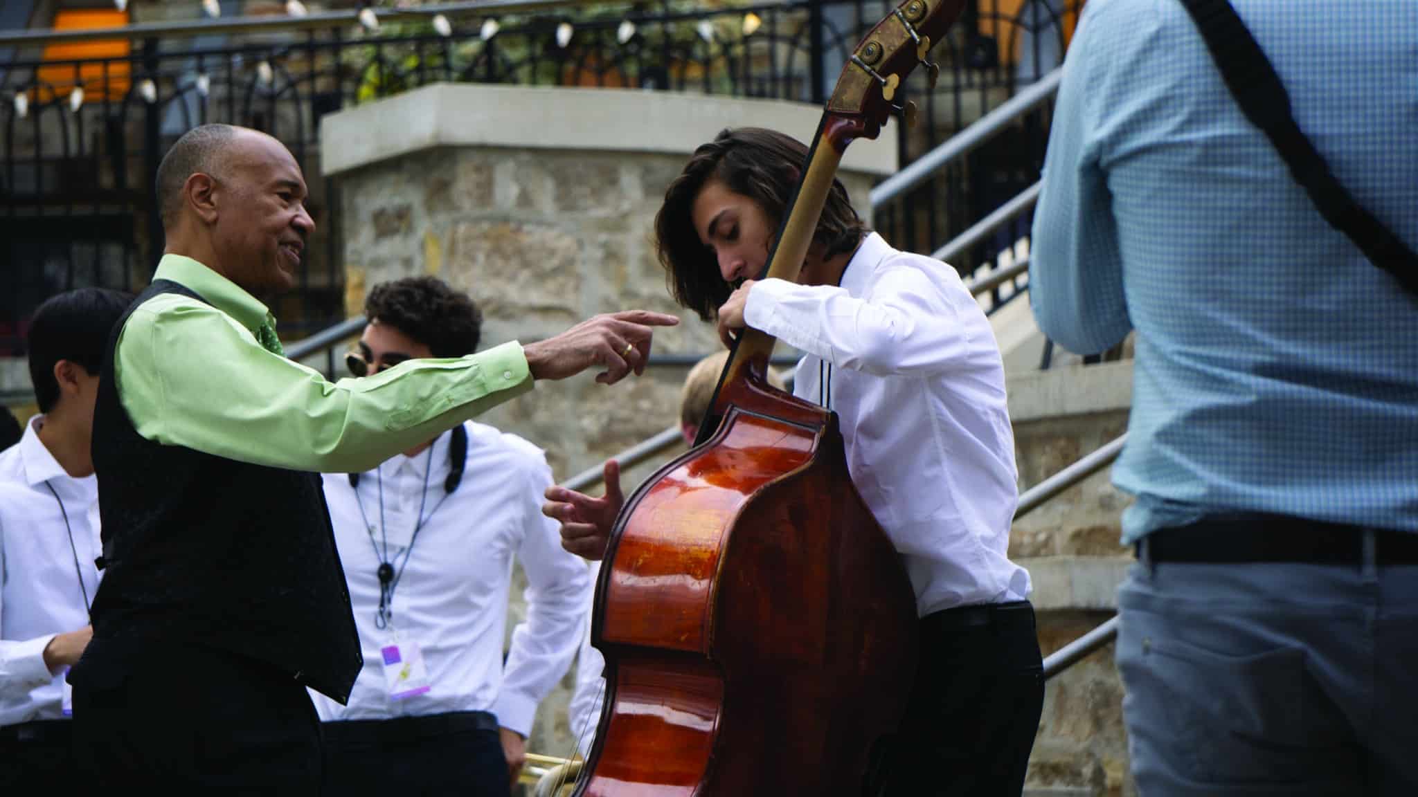 A man is holding a cello and another man is holding a bass.