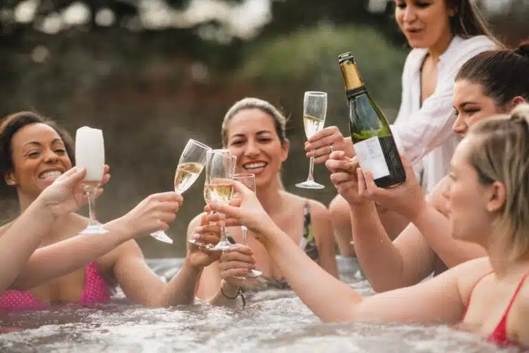 A group of women in swimsuits sit in a hot tub in Vail, clinking full champagne glasses in a toast.