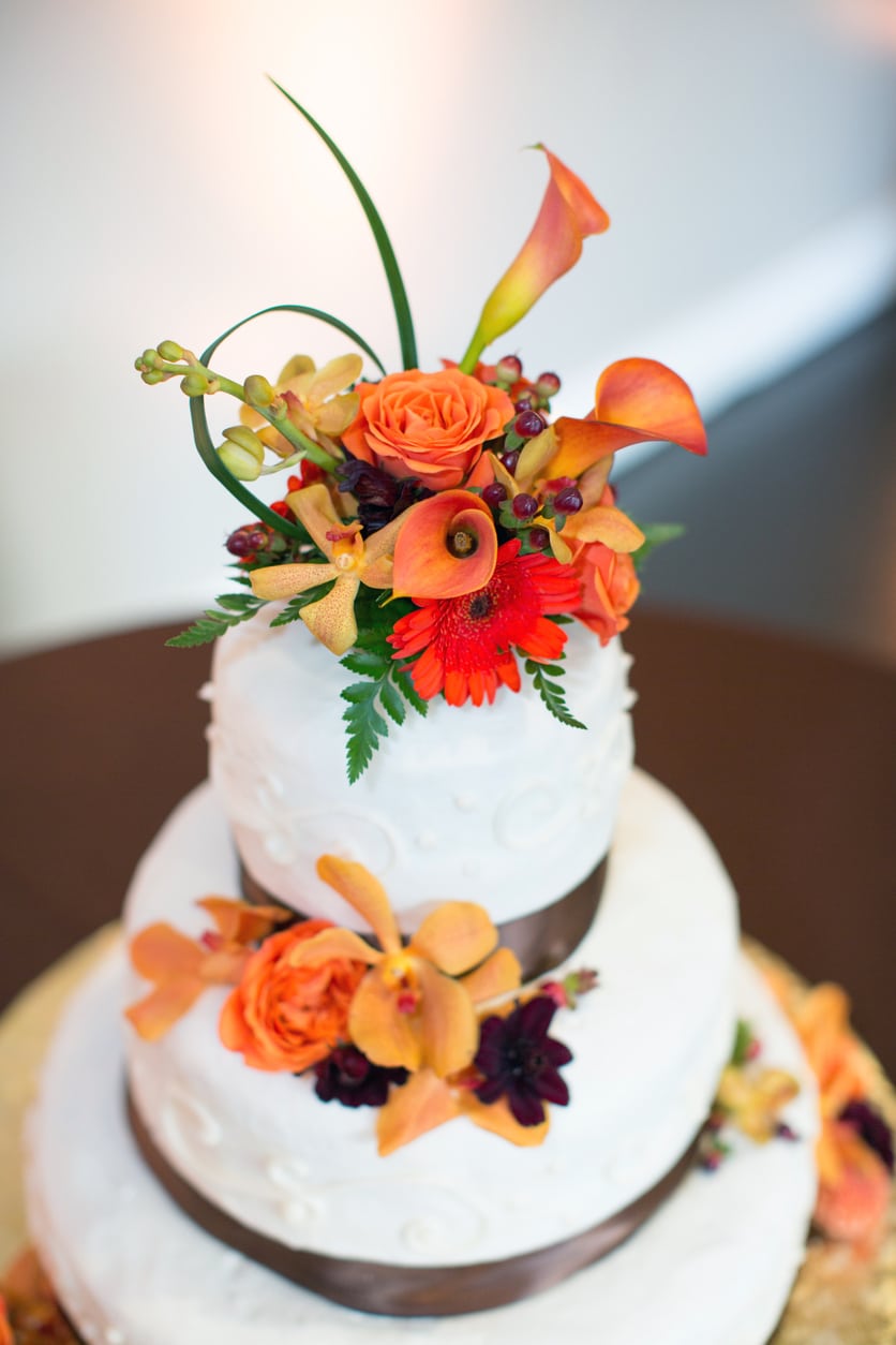 A three-tiered wedding cake is decorated and topped with flowers in tones of reds and oranges.