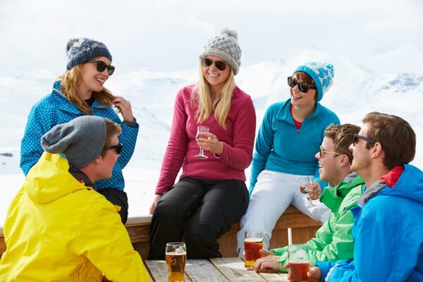 Friends enjoying apres-ski on Vail Mountain. They wear colorful winter clothing and smile.