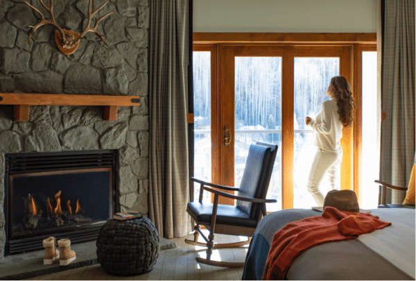 A woman standing in front of a fireplace in a hotel bedroom in Vail. She looks out the window at a winter landscape.
