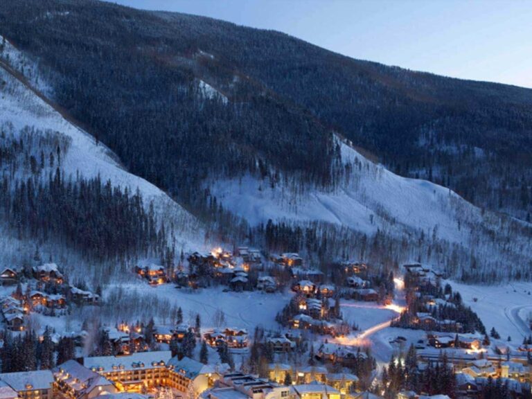 East Vail, Colorado, is quiet and peaceful at the base of a mountain at dusk. Yellow lights in the buildings illuminate the area.