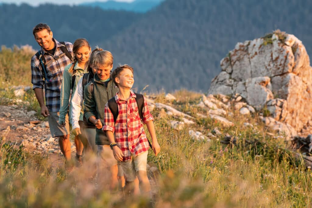 A smiling family of four hiking in the Vail mountains during sunset. Around them in the background are groves of pine trees.