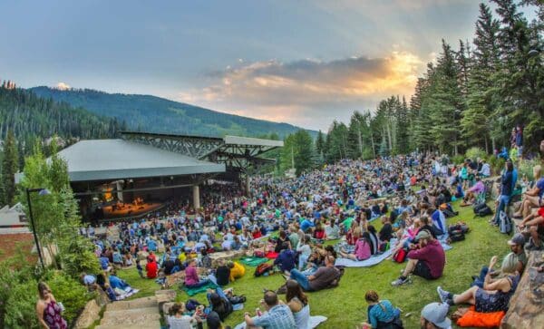 The audience settles in on blankets at sunset for a Bravo! Vail Music Festival performance at Gerald R. Ford Amphitheater. Mountains and pine trees ring the outdoor venue.