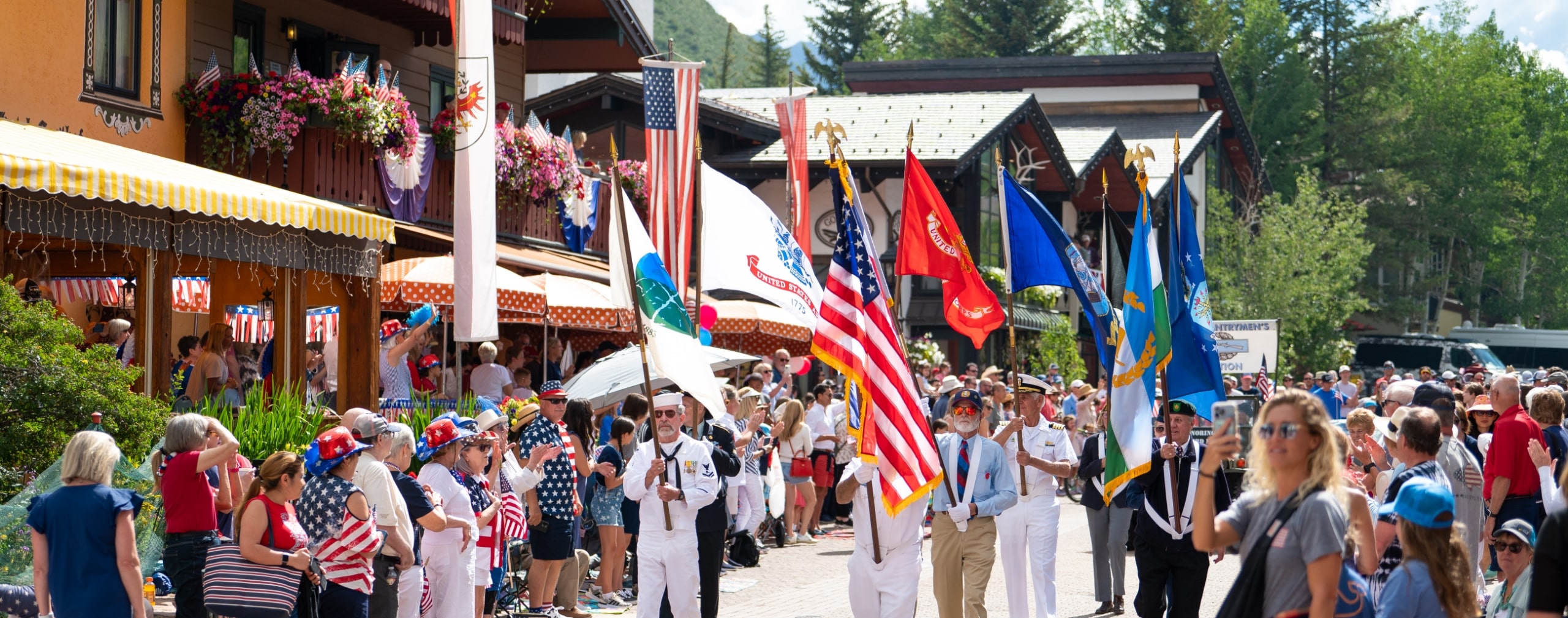 People parade through Vail Village with various flags around a crowd dressed in red, white and blue during the Fourth of July parade in Vail, Colorado.