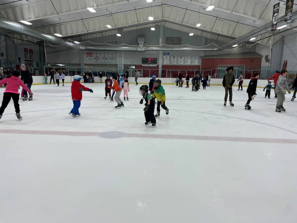 a group of kids skating on an indoor ice rink.