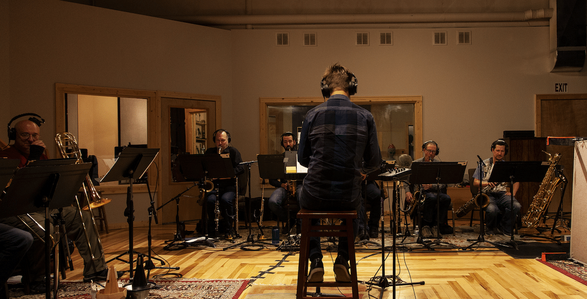 Five jazz musicians practicing in a studio with a conductor leading the group