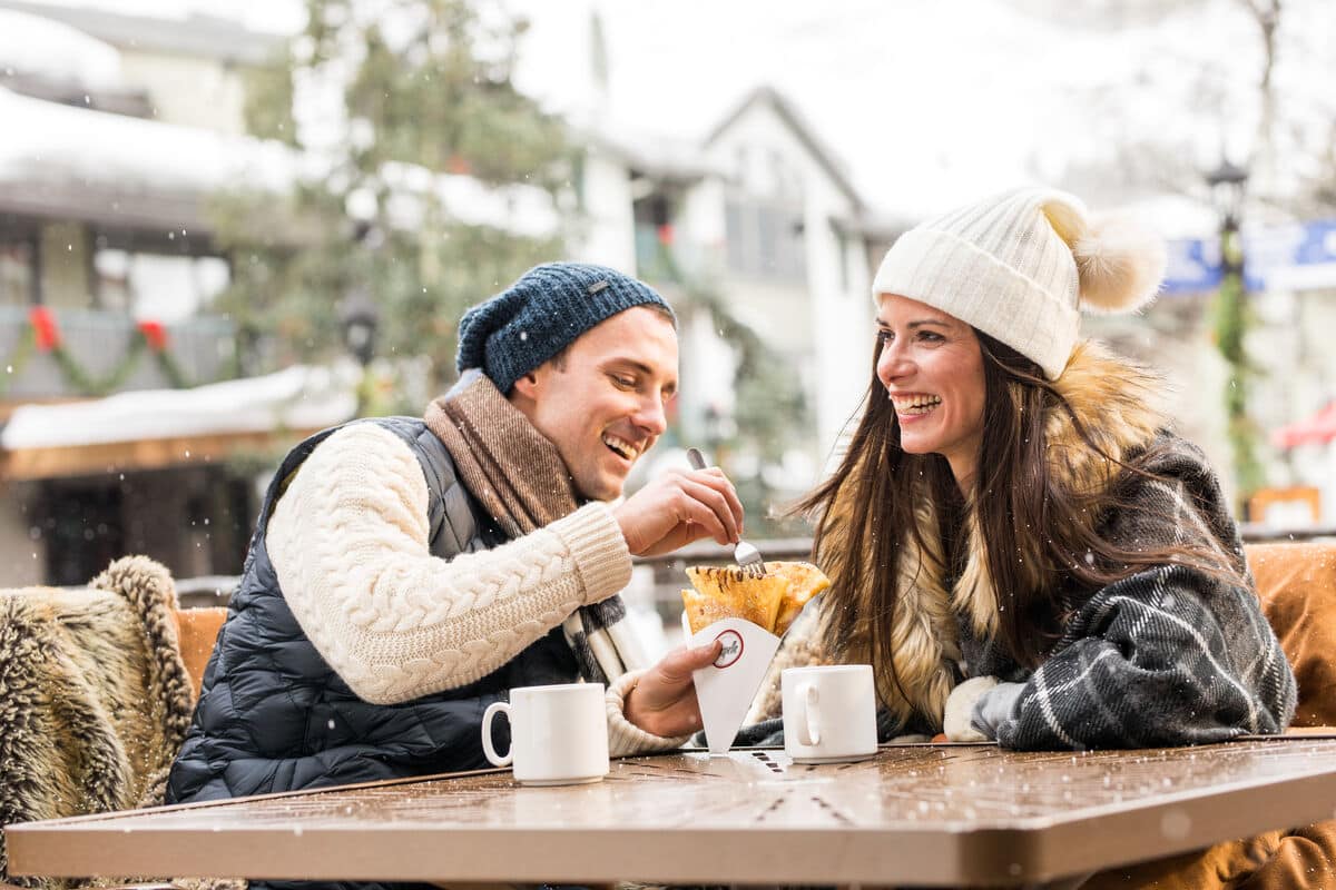 Couple sitting outside in Vail with coffee and crepes in the winter