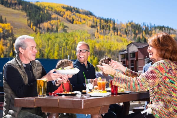 A multi-generational family dines outside in fall. There are food and drinks on the table.