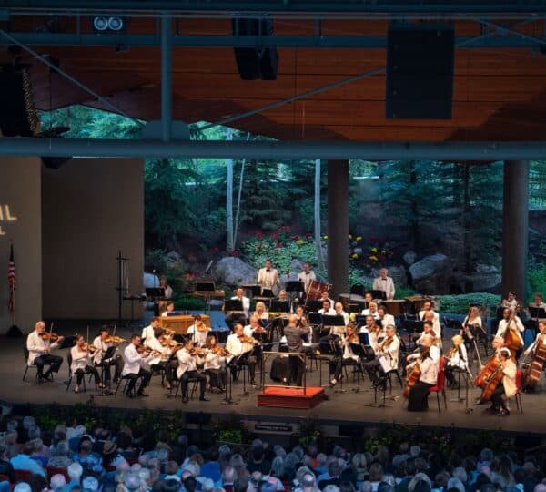 An orchestra plays on a stage with nature in the background at The Amp in Vail, Colorado.