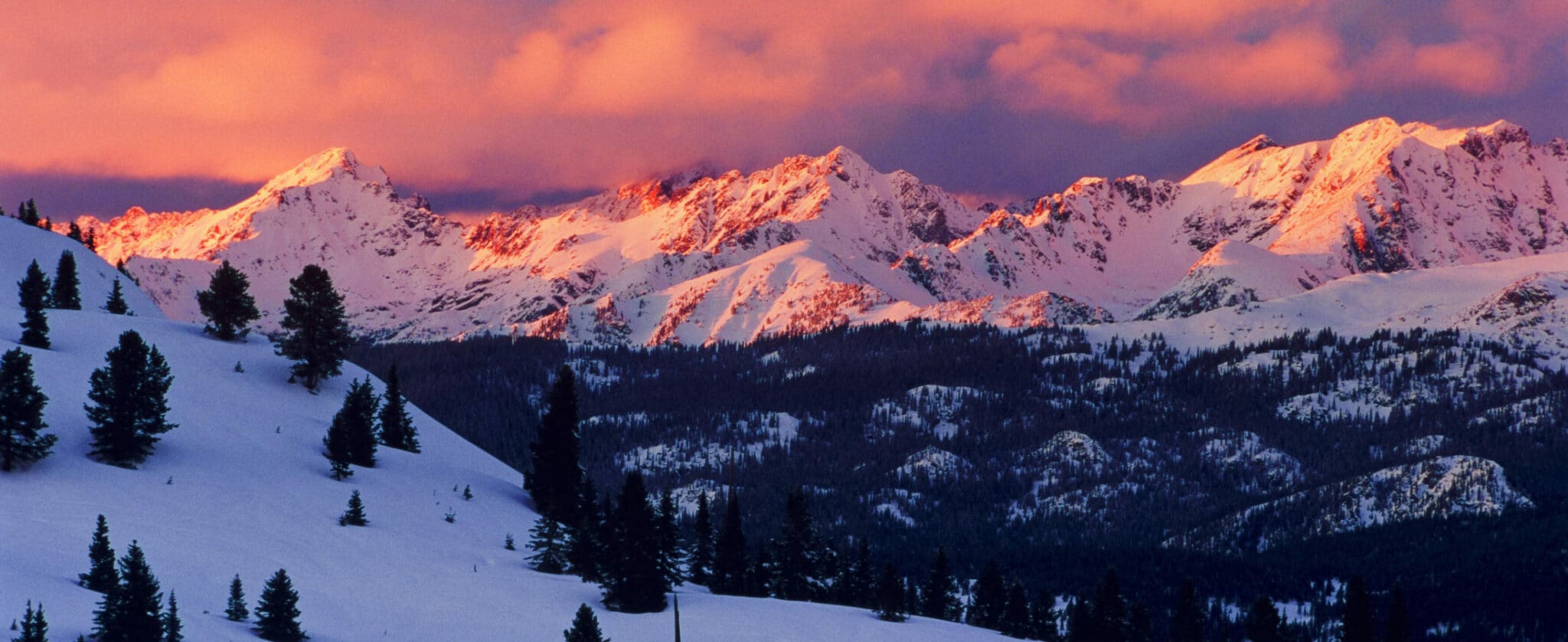The mountains of Vail Colorado are covered in a blanket of snow. As the sun goes down, the sky and snow are painted in tones of pink.
