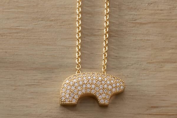 A yellow-gold Golden Bear necklace features a bear pendant studded with diamonds. The sparkling necklace lies flat on a light-colored wood surface in Vail, Colorado.
