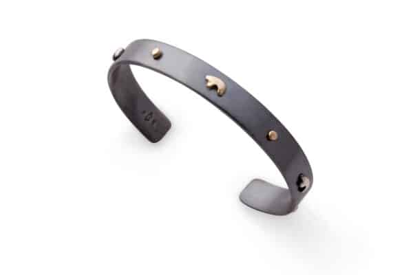 A Golden Bear leather cuff is featured on a white background. The cuff from Vail has a design of yellow-gold and oxidized-silver bears and metal studs.