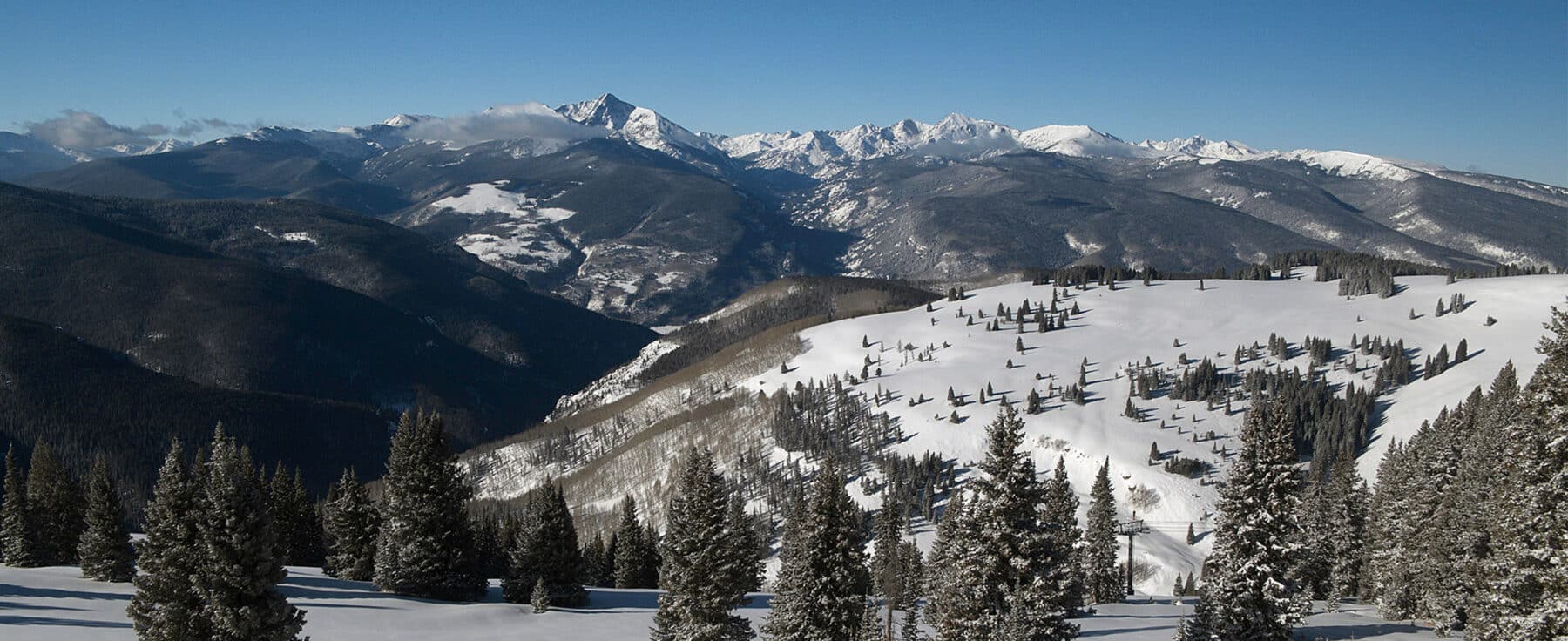 The mountains of Vail are covered in pine trees and a fresh layer of snow. The sky above is a bright blue without any clouds.
