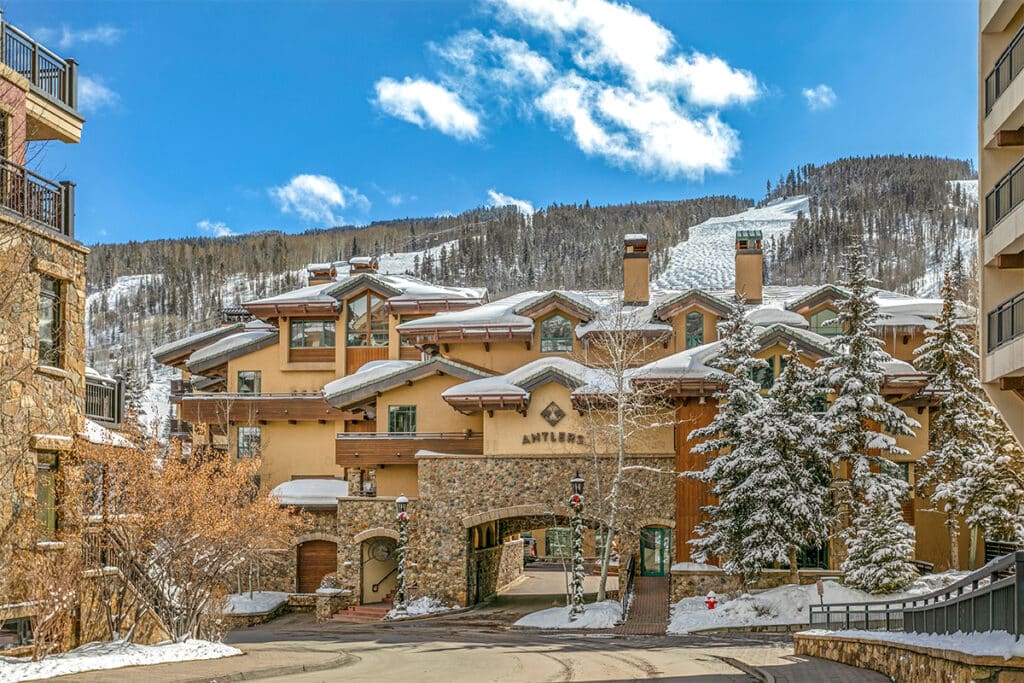 The Antlers at Vail has a blanket of snow on its roof. The forested peaks of Vail Mountain are seen in the distance.