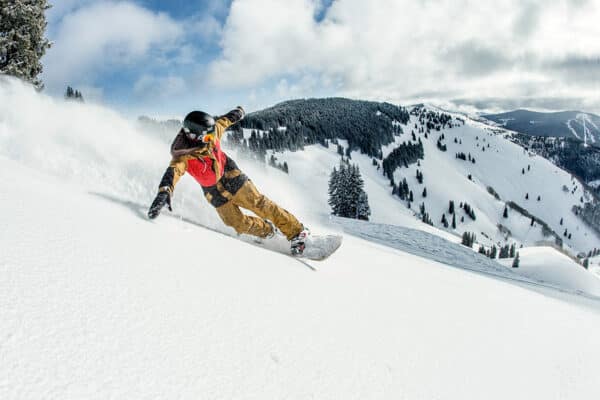A snowboarder wearing a winter jacket, helmet and goggles, skillfully makes their way down the snowy Vail Mountain slope leaving a layer of snow-dust in the air.