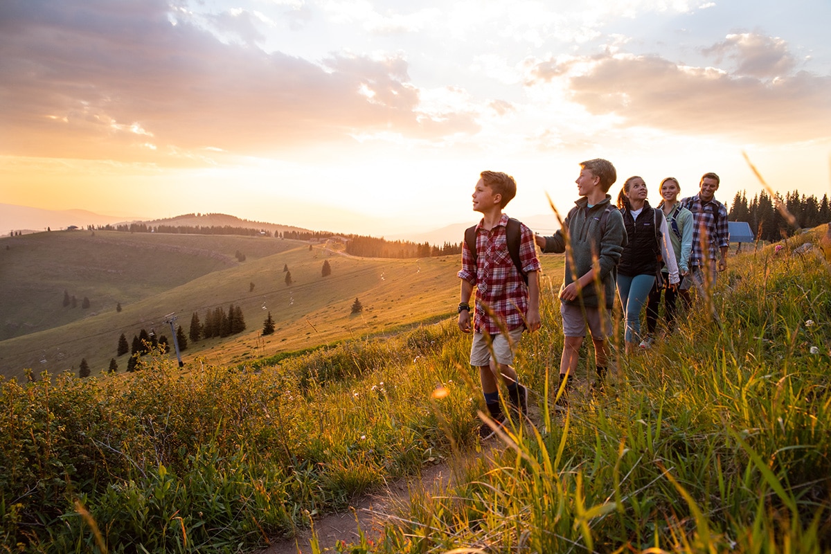 A family of hikers pauses to look up at the sky as the sun begins to set near the ski chair lift on Vail Mountain in Colorado.