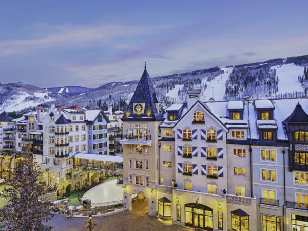 The Arrabelle at Vaill Square stands before snow-covered runs at Vail Mountain at dusk.