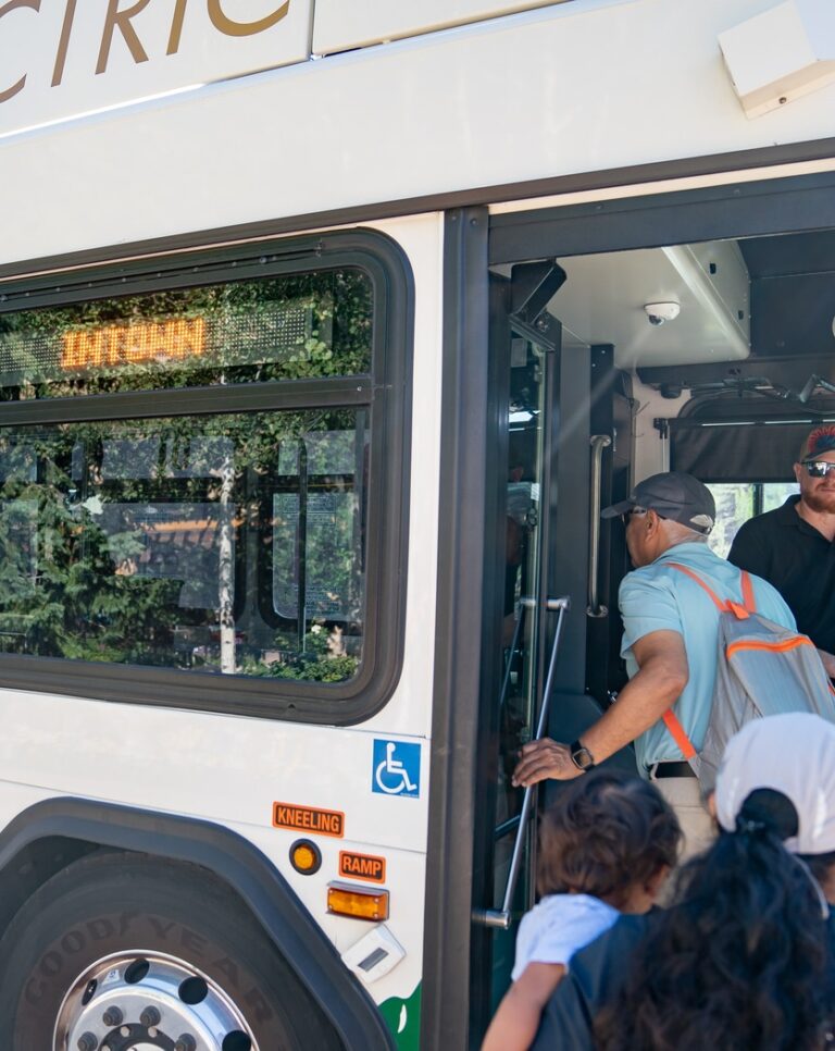 A Town of Vail bus is stopped and people board through its door in summer.