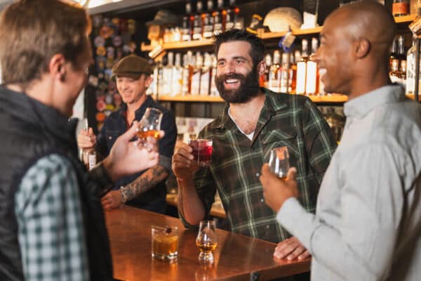 Three friends smile and laugh as they drink glasses of whiskey at 10th Mountain Whiskey & Spirits in Vail, Colorado.