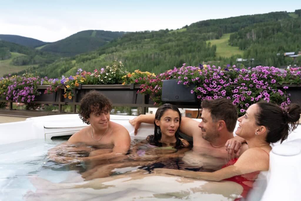 Family of four sitting in a hot tub with a mountain background