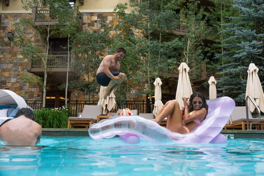 Dad doing a cannonball into a pool with daughter afraid of getting splashed.