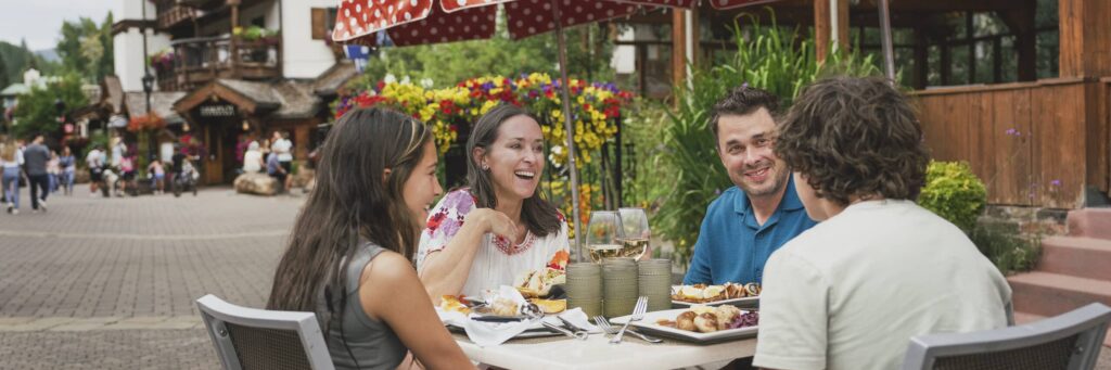 Two parents and their teenage son and daughter sit smiling at a table in the Vail Village dining on a variety of dishes.