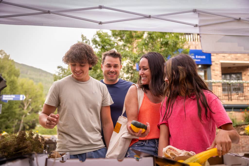 Family of four checking out fruits and vegetables under a tent at the farmers market