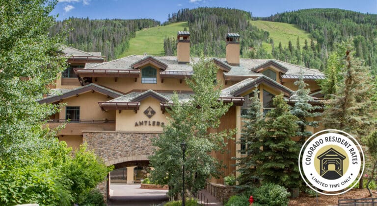 Image of a hotel entrance surrounded by trees in the foreground with a ski mooutanin in the background. A "Colorado Resident Rates - Limited Time Only" badge appears on the bottom right of the image.