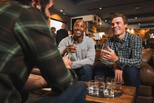 Three people sit around a table at 10th Mountain Whiskey & Spirits sampling sipping glasses of whiskey near Vail, Colorado.