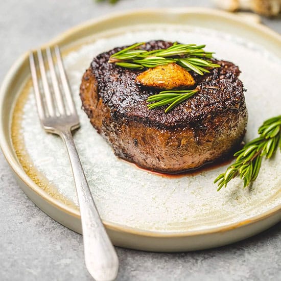 Close-up view of a steak on a plate topped with rosemary and garlic in Vail, Colorado.