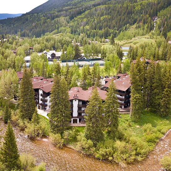 Aerial view of condos and tennis courts at Vail Racquet Club Mountain Resort, surrounded by evergreen trees and mountains in Vail.