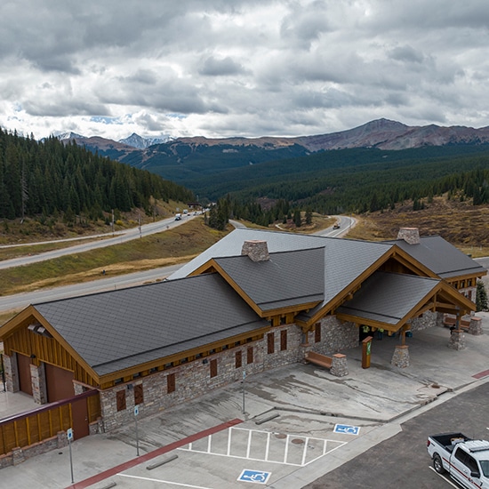 View from above of Vail Pass Rest Area, a wood building with a grey roof and I-70, trees and mountains in the background.