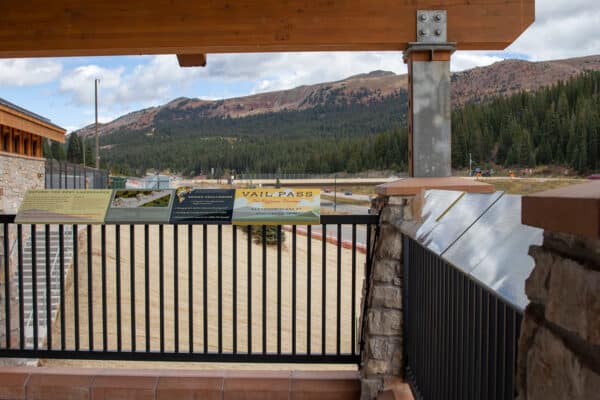 A viewing deck at Vail Pass Rest Area in Colorado with signage, looking out to mountains and trees