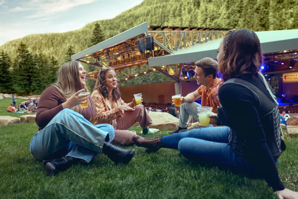 Group of young people enjoy beverages at an outdoor amphitheater during a concert in vail